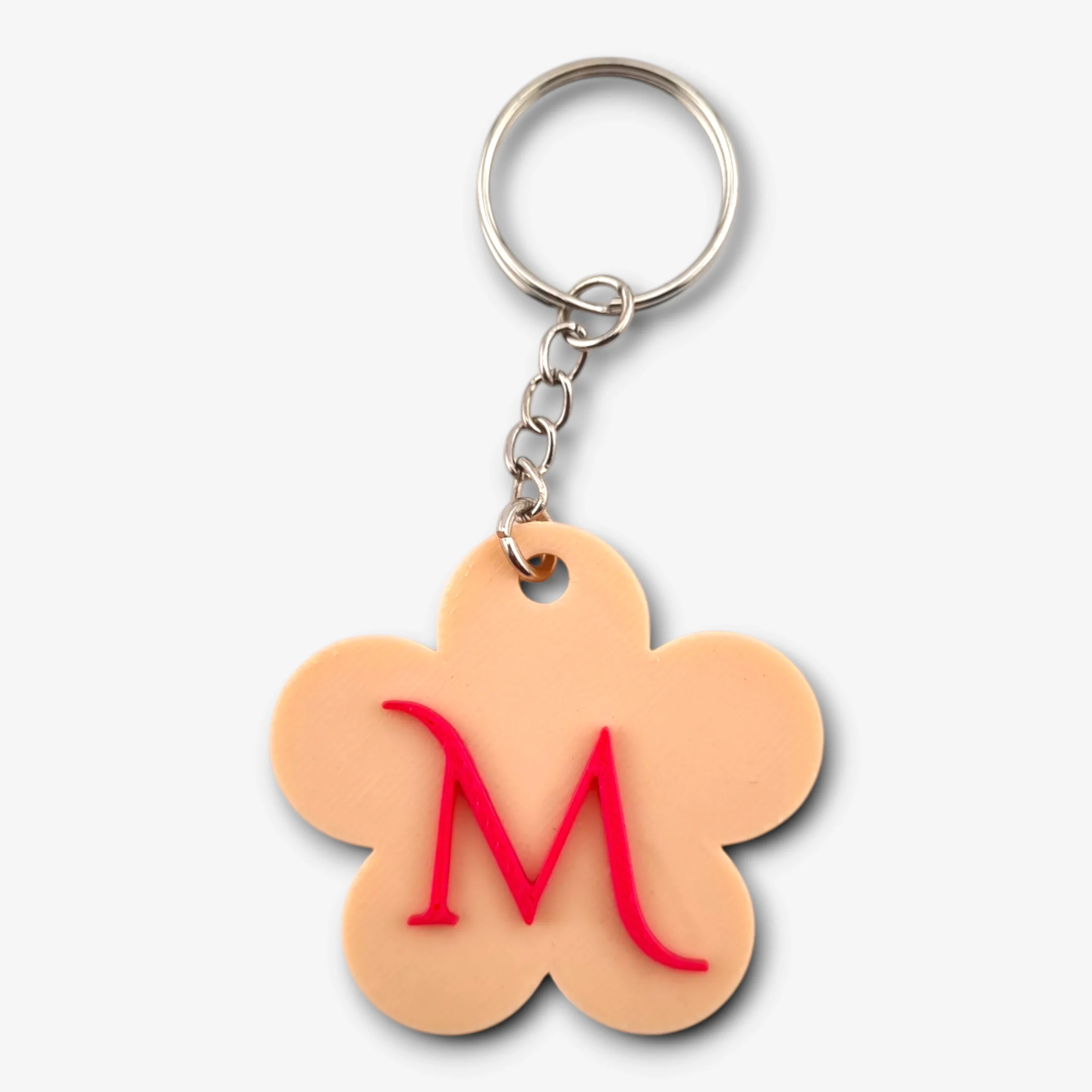 A peach-toned flower-shaped keychain featuring a bold red initial 'M' in the center.